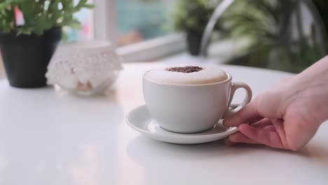 closeup shot of a hand delivering a beautiful cappuccino to an elegant coffee shop table