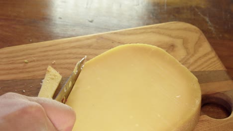 delicious hard dry cheese is sliced with small knife on cutting board