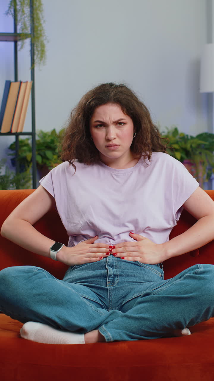 Sick ill woman suffering from period cramps stomach ache menstrual pain lying on sofa at home room