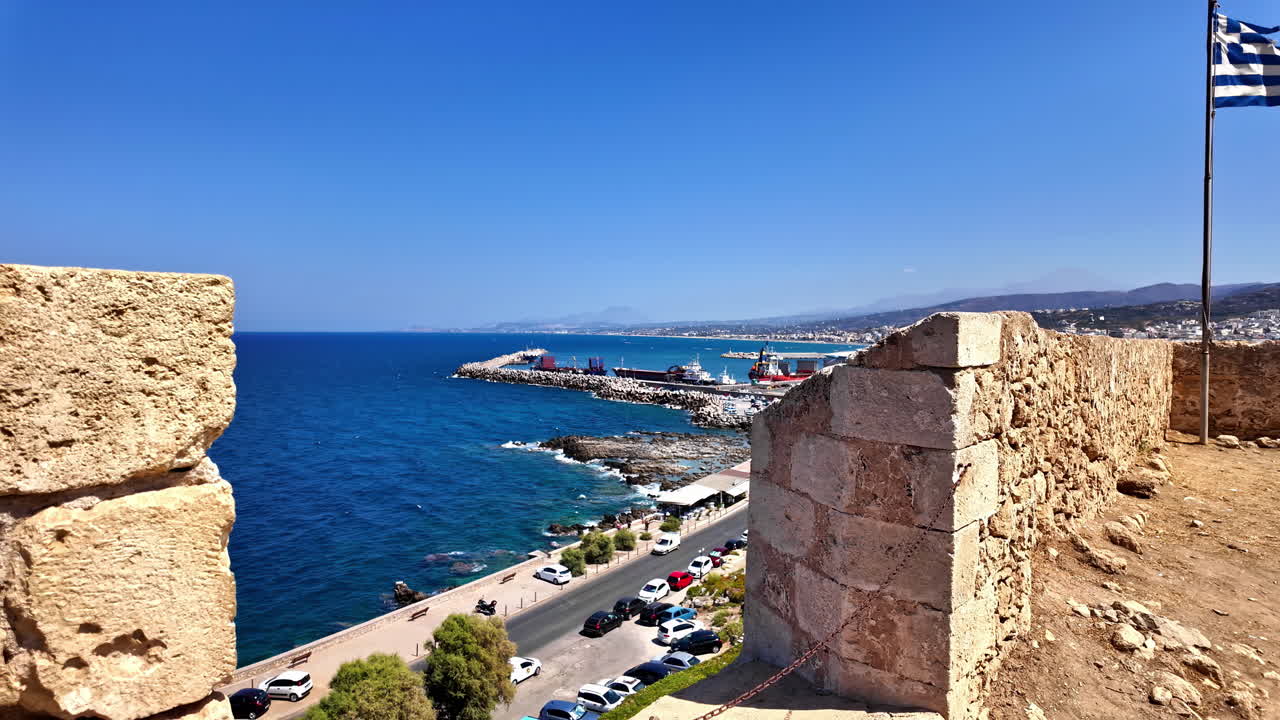 Pan shot capturing beautiful seascape from a viewpoint of Venetian Fortezza Castle with Greek flag waving on a windy day in Greece.