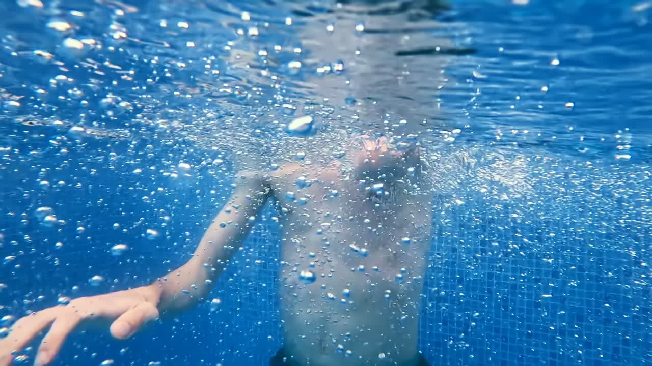 Tall young man jumping into the pool. Slow motion. UUnderwater view. Air bubbles in foreground