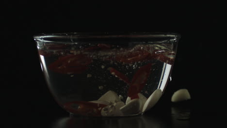 cámara lenta de ajo cayendo en un recipiente con agua y chile