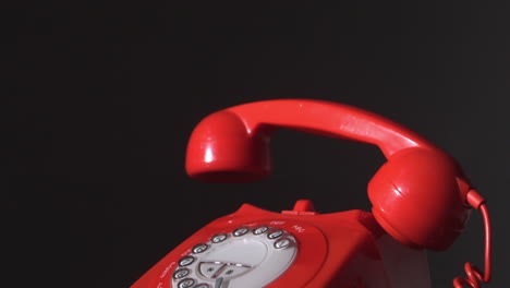 red phone receiver dropping on dial phone on black background