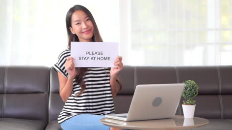 asian woman social distancing covid-19 campaign holding stay at home paper page in apartment interior