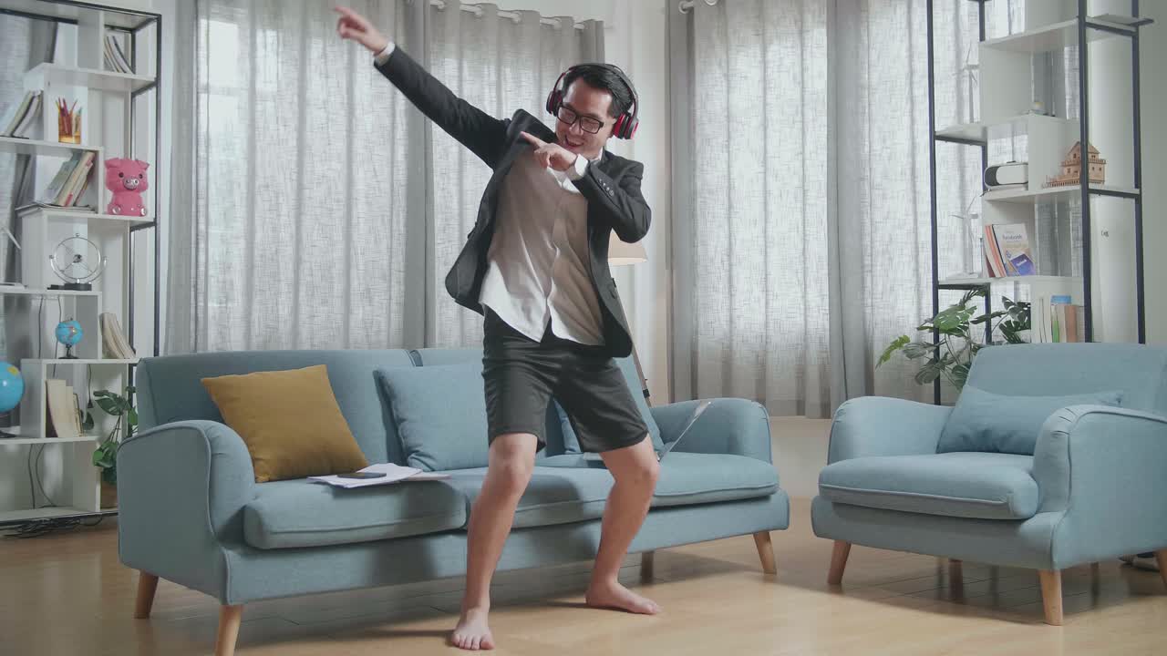 집에서 노트북으로 일한 후 헤드폰으로 음악을 듣고 춤을 추는 재과 쇼트를 입은 아시아 사업가