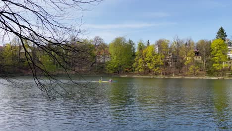 Two-kayakers-kayaking-on-dam-or-lake-in-Liberec,-Czech-Republic,-trees-and-brunches-in-foreground