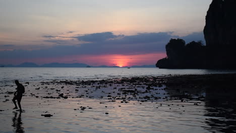 Silhouette-Eines-Fotografen,-Der-Einen-Sonnenuntergang-Auf-Dem-Meer-Mit-Einem-Langen-Boot-Einfängt,-Das-In-Railay-Thailand-Vorbeifährt