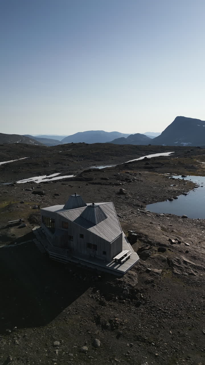 Vertical aerial shot panning around showing Rabothytta cabin, situated on the edge of Okstindbreen glacier, with views of the Okstindan mountain range in the distance. Korgen, Norway