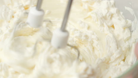 close up shot of whipping heavy cream with melted white chocolate in glass bowl using hand mixer