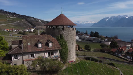 Slow-aerial-subject-reverse-shot-of-an-old-winery-in-the-hills-of-the-countryside-near-Lutry,-Switzerland-on-a-sunny-day