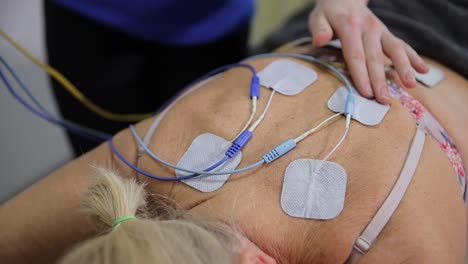 woman receiving electrode massage therapy for relaxation and pain relief. a woman is undergoing electrode massage therapy lying on a bed with electrical pads on her back. the treatment aims to provide relaxation and pain relief