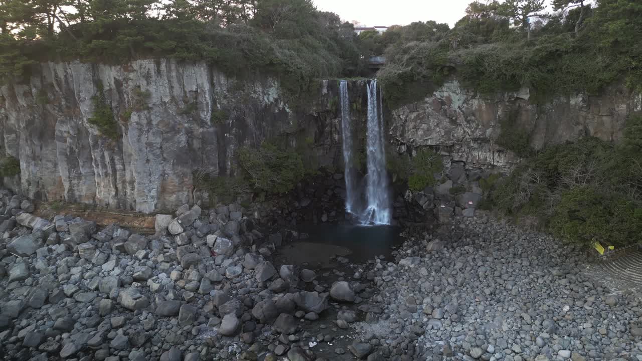 Drone aerial view in South Korea flying in front of a waterfall over the sea rocky area backwards jeju island