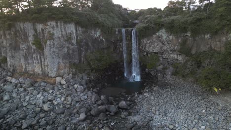 drone aerial view in south korea flying in front of a waterfall over the sea rocky area backwards jeju island