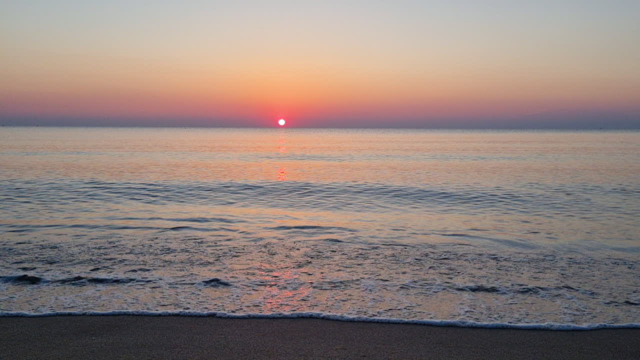 일출-1의 모래 해변에서 잔잔한 물 표면과 바다 파도가 튀다