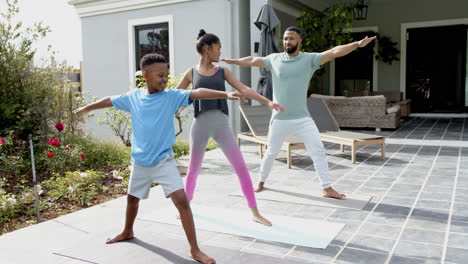 happy african american father, son and daughter practicing yoga standing in garden, slow motion