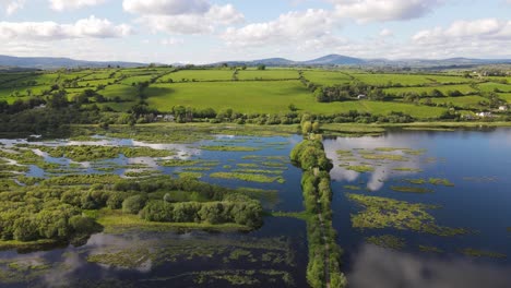 sunny day with white cloud reflections in the dark blue waters of river lee and green footpath in the gearagh, ancient petrified and submerged forest during high tide