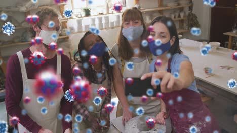 animation of covid cells over diverse friends in face masks taking selfie at pottery workshop