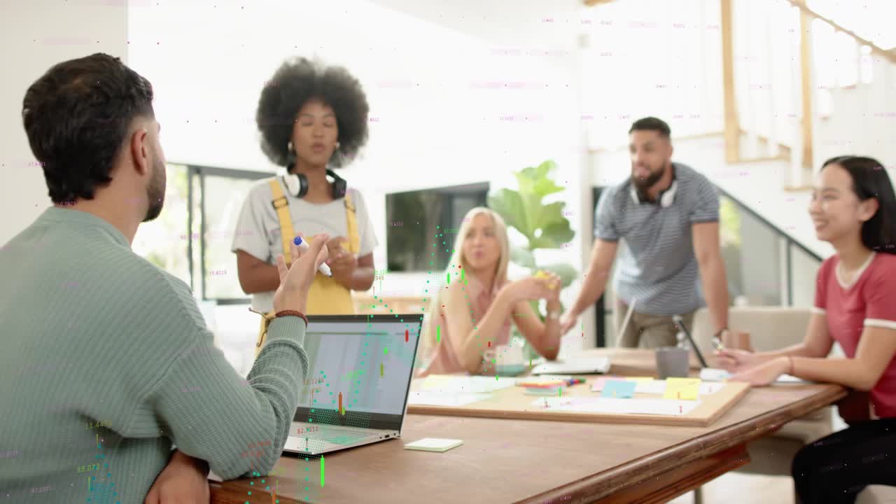 Presenter leaning on table then standing while explaining creative plan, team consulting laptops