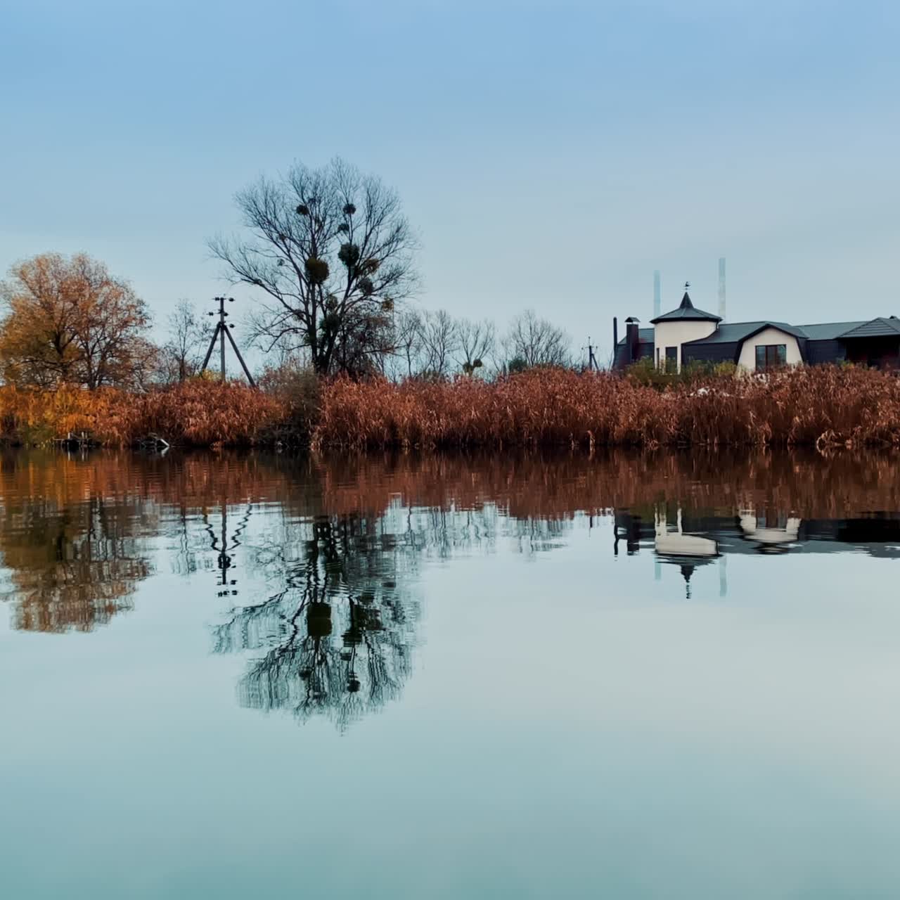 Looking at the dry waterfront from the river. Metal bridge connecting the banks and beautiful modern house near the water. Autumn nature out of big city
