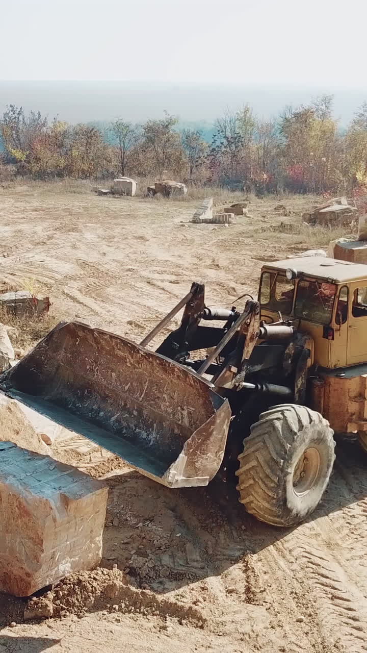 professional yellow bulldozer with a bucket is working in the quarry with stones on the background of sand. Close-up. Vertical video