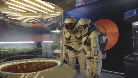 astronauts monitor plants in a space greenhouse