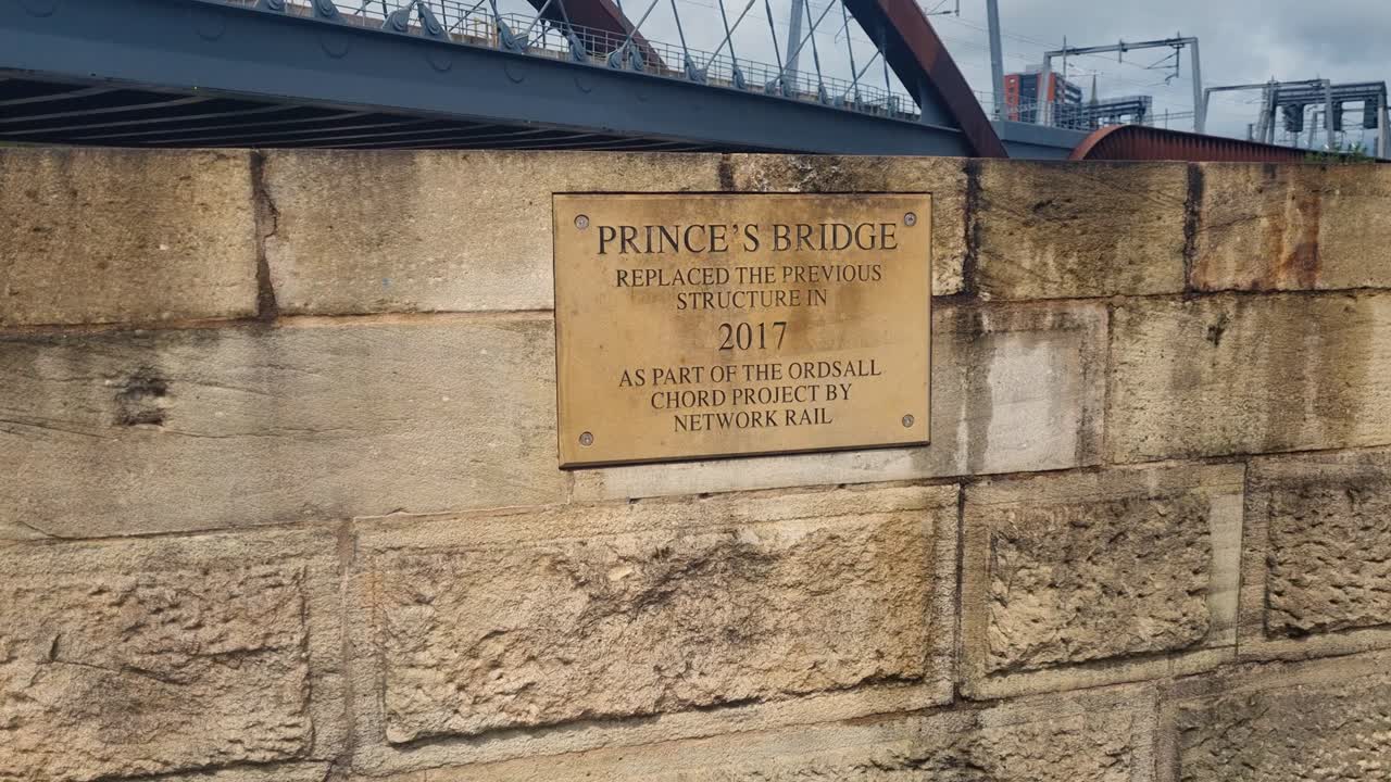 Prise de vue du Princes Bridge à Manchester sous un ciel couvert, mettant en évidence la structure du pont et la signalisation, capturant l’infrastructure urbaine et le caractère industriel de la ville