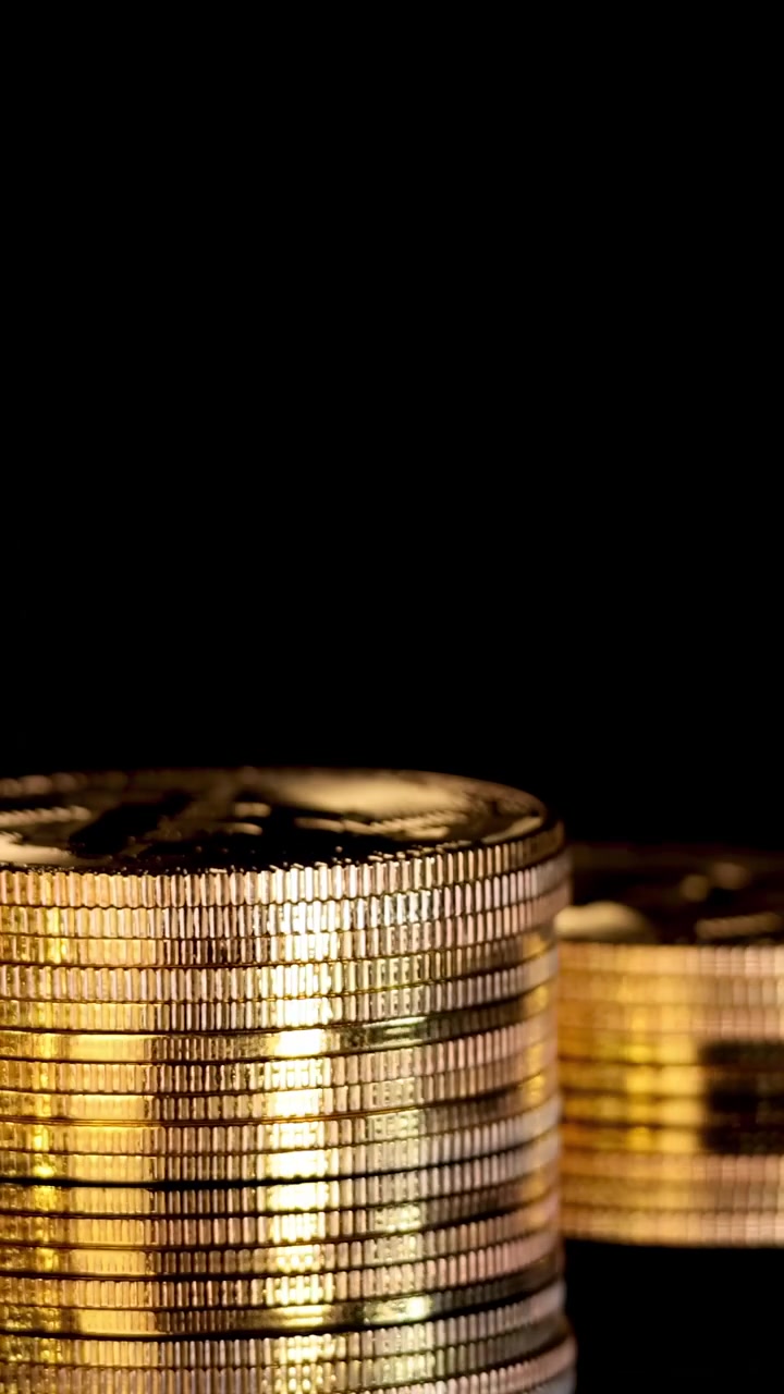Gold cryptocurrency coin rotates atop stacked coins, dramatic lighting, close-up, black background, smooth camera movement