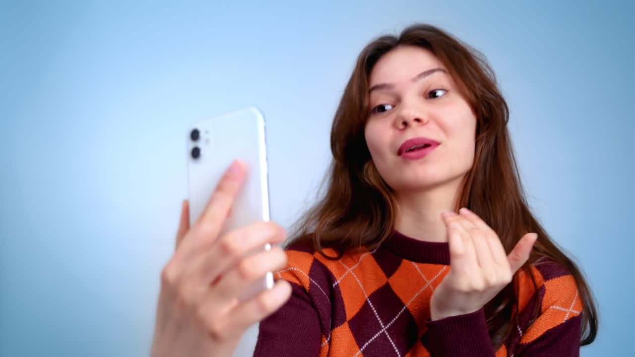 Young woman talking while filming herself on the phone and gesturing, showing a lot of emotions on a grey background