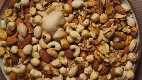 close up overhead shot of nuts falling into bowl containing cashews dry roasted peanuts pistachio walnuts and hazelnuts