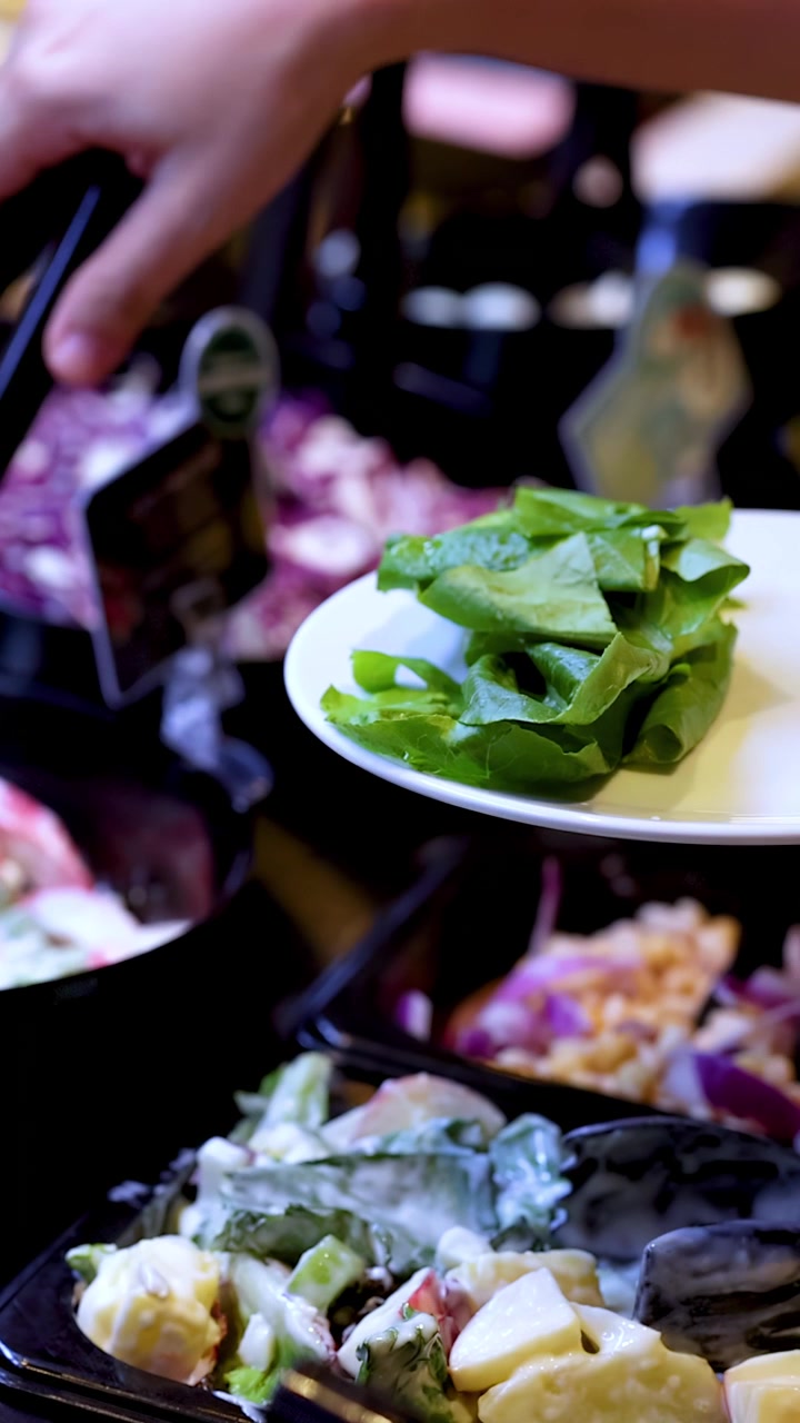 Una mano usa le pinze per servire insalata verde fresca su un piatto a un buffet di ristorante.