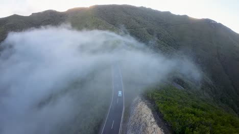 car driving on a mountain road surrounded by forest inside a cloud