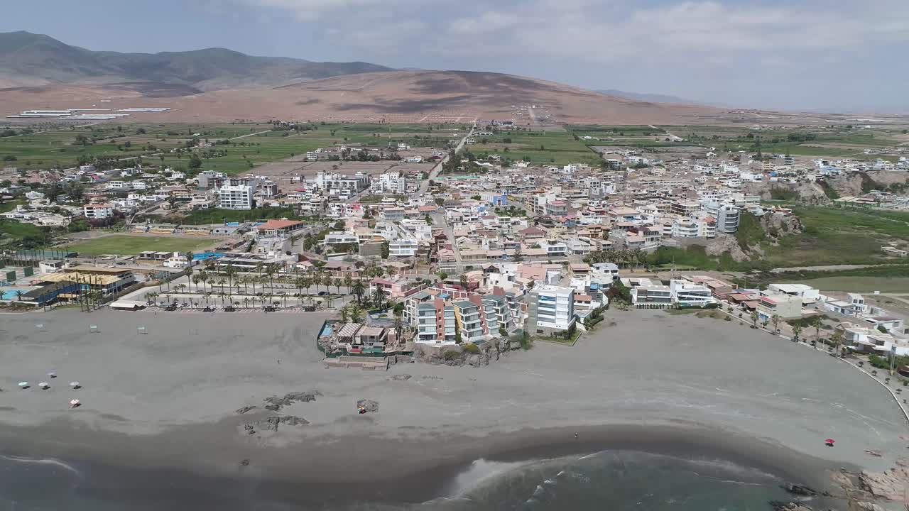 A breathtaking aerial view of a coastal town, featuring a sandy beach, ocean waves, and a stunning mountain backdrop. Perfect for travel, real estate, and tourism projects. Mollendo, Arequipa, Peru.