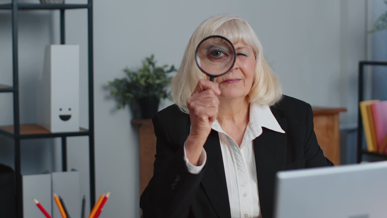 Senior business woman looks through a magnifying glass investigate examine analyzing reading