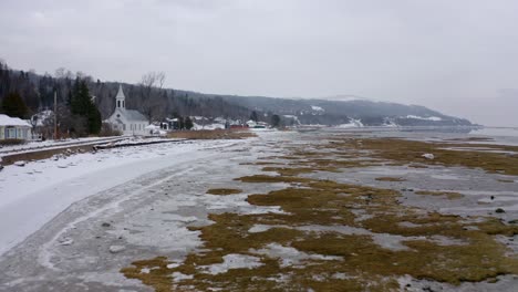 drone flying over the frozen river on the edge of a small village in wintertime