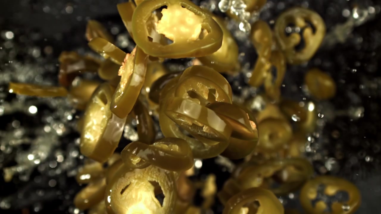 Fette di peperoncino jalapeño verde che galleggiano nell'acqua al rallentatore.