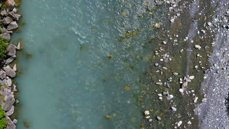 top down view of rocky river bank with blue fresh water flowing downstream on sunny day, aerial