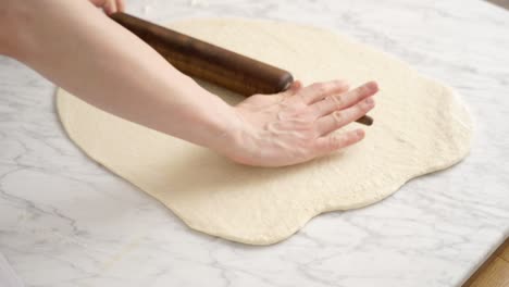 crop baker rolling out dough in kitchen