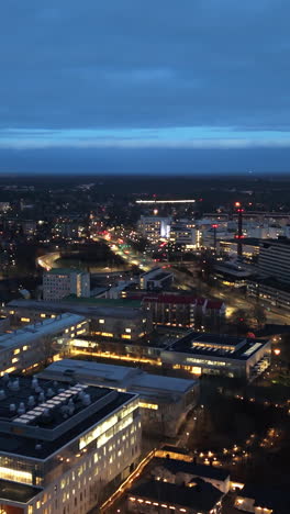 vertical aerial approaching the illuminated kupittaa business hub, dusk in turku