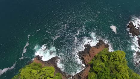 overhead hover of rugged jungle island point with crashing waves on rocks