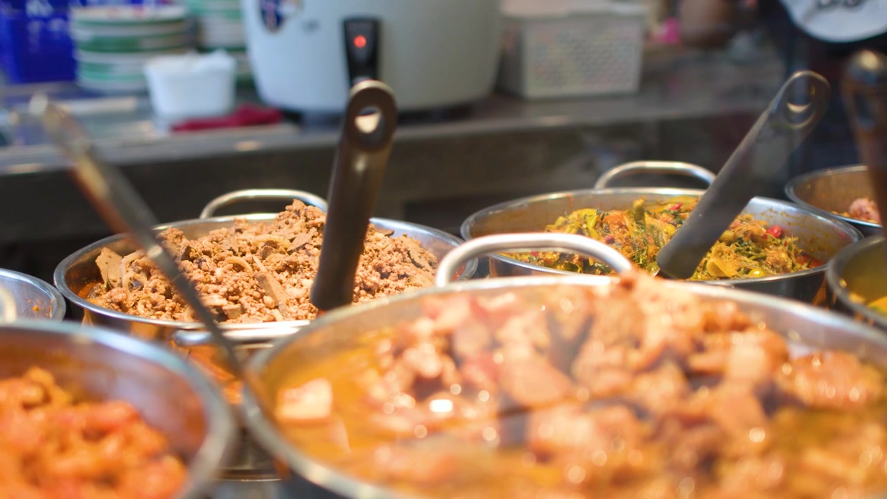 Inquadratura ravvicinata a mano libera di vari curry e stufati tradizionali della Thailandia del Nord in una caffetteria.