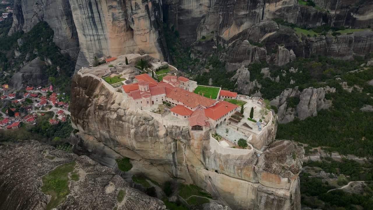 Wide aerial of Meteora monastery nestled on cliff amid forested Greek landscape