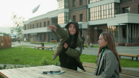 Kid throws paper kite playfully as it flies back toward his head, making his sister laugh while he claps hands in amusement, enjoying fun outdoor moment filled with energy and joy