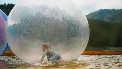 Girl-crawls-inside-water-sphere-floating-in-pond-in-park