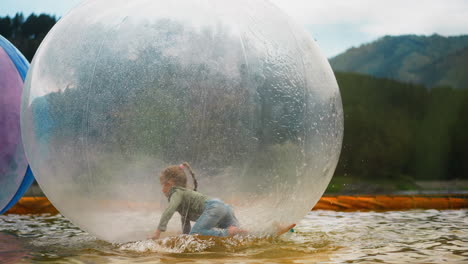 girl crawls inside water sphere floating in pond in park