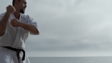 sporty man practicing karate fighting on beach. bearded athlete workout outdoors