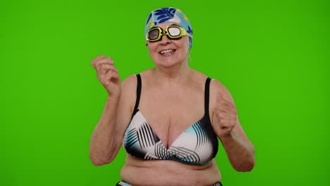 Senior-pensioner-woman-tourist-in-swimsuit-bra,-swim-goggles-and-hat-dancing-celebrating,-smiling