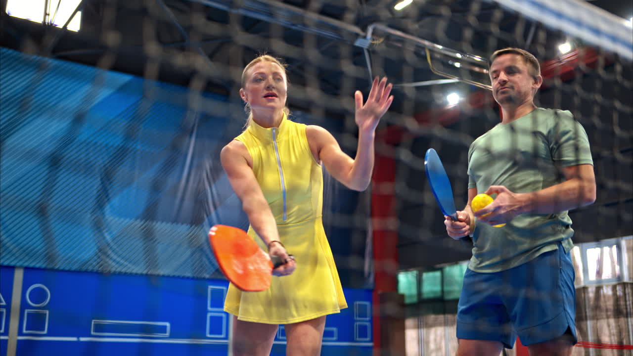 A man teaching a woman how to play pickleball in an inside court