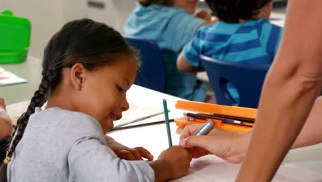 Teacher-helping-schoolgirl-with-her-homework-in-classroom