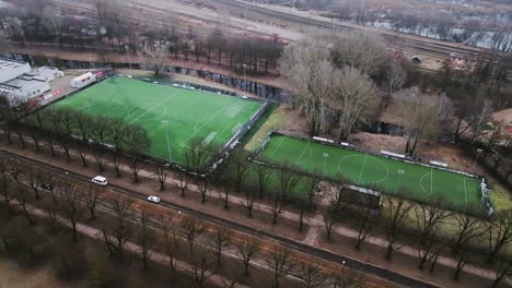 park with green soccer fields, tree-lined roads, and nearby railway track, riga
