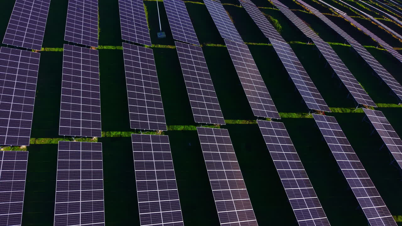 Vasto campo di energia solare che brilla sotto un'intensa luce solare, con numerosi pannelli solari disposti in modo uniforme su un terreno verde.